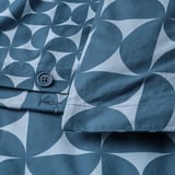 Detail tmavě modrého vzorovaného povlečení se zapínáním na knoflík. Kruhy a trojúhelníky tvoří opakující se moderní design z poloviny století.