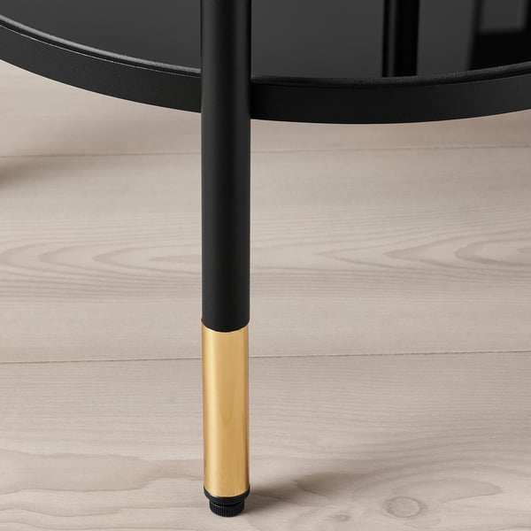 Detailní záběr na elegantní, moderní nohu stolu. Černý kov se zlatou základnou, na dřevěné podlaze.