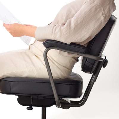 Osoba sedící na ergonomické kancelářské židli, nastavitelná bederní opěrka.