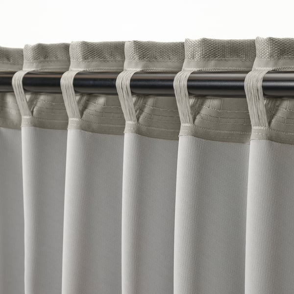 Detail světle šedých závěsů s hlavičkovací páskou a háčky, připravených k instalaci prutu.