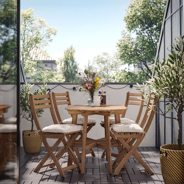 Útulný balkon s dřevěným stolem, židlemi a řetězovými světly pro venkovní stolování.