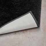 Černý roh koupelnové předložky s bílým latexovým podkladem, který ukazuje měkký vlas a bezpečný úchop.
