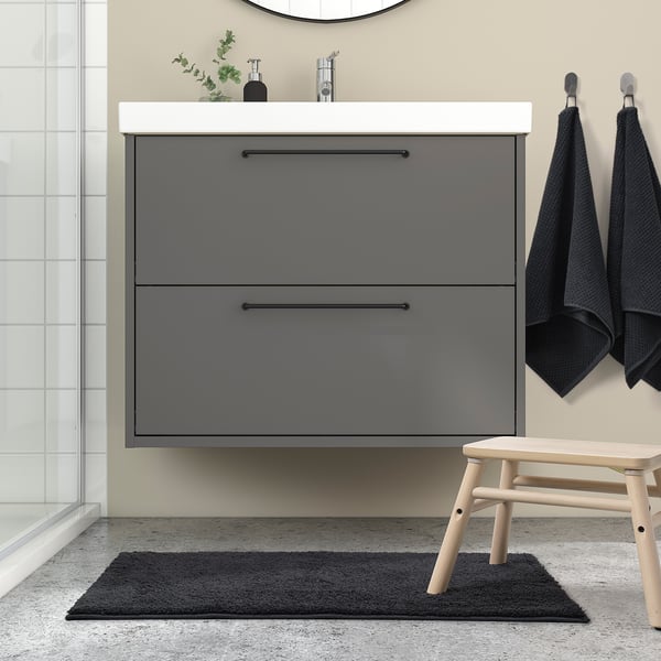 Moderní koupelna s šedou koupelnovou předložkou BACKMÅRA, elegantním toaletním stolkem a ručníky. Podložka se vejde pod umyvadlo s černými akcenty.