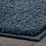 Detailní záběr plyšové, tmavě modré koupelnové předložky se silnou, měkkou strukturou a latexovým podkladem.