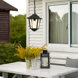 Černá závěsná lampa nad stolem na verandě s květinami.