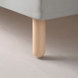 Detailní záběr na lehkou dřevěnou nohu stolu na podlaze, která ukazuje jemné řemeslné zpracování a přírodní povrchovou úpravu.
