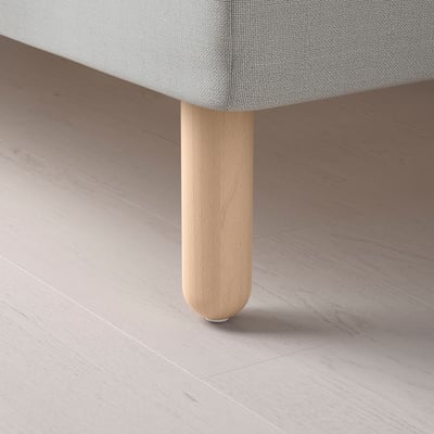 Detailní záběr na lehkou dřevěnou nohu stolu na podlaze, která ukazuje jemné řemeslné zpracování a přírodní povrchovou úpravu.