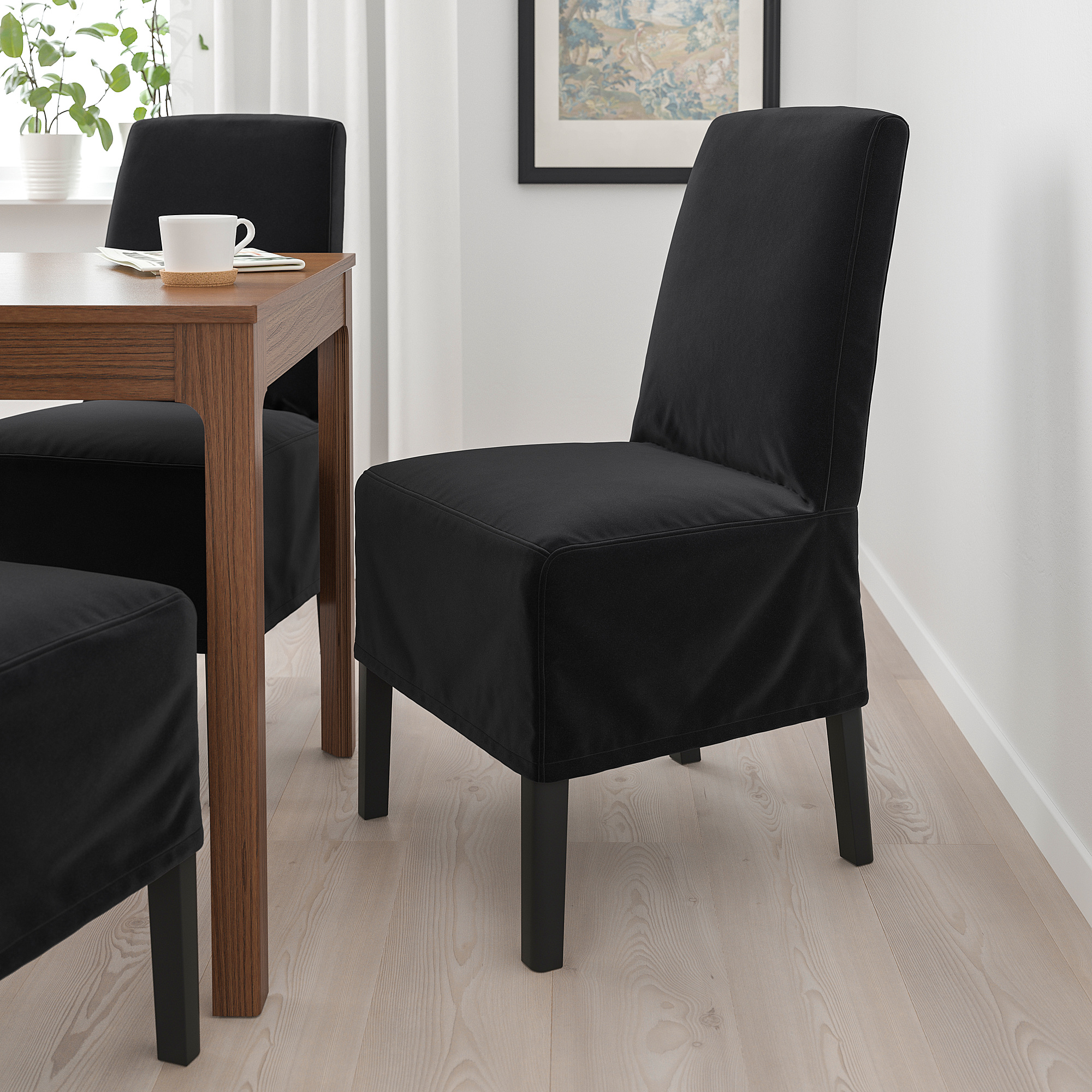 Moderní černá čalouněná židle, elegantní design, úhledně se vejde pod dřevěný stůl, ideální pro stolování.