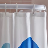 Průhledný, bílý sprchový závěs úhledně visí na stříbrné tyči; viditelné jemné záhyby a jemný design.