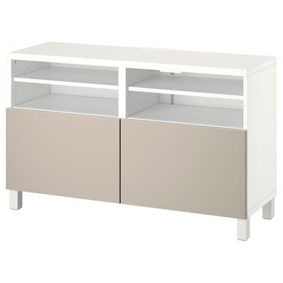 Bílý TV stolek BESTÅ s béžovými dvířky. Obsahuje čtyři nastavitelné police pro ukládání, které poskytují moderní a funkční design.