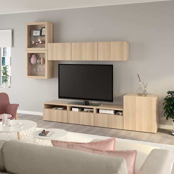 Moderní obývací pokoj s TV jednotkou BESTÅ, TV s plochou obrazovkou, vázami a dekoracemi. Šedé stěny, béžová pohovka, růžové akcenty, konferenční stolek s časopisem a svíčkou.