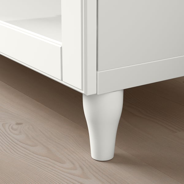 Moderní bílý úložný díl s elegantním designem, nastavitelnými policemi a stylovými nohami, umístěný na dřevěné podlaze.