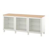 Bílý příborník IKEA BESTÅ se třemi skleněnými dvířky a dřevěnou deskou. Skříňka má moderní design s nastavitelnými policemi pro ukládání.