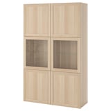 Světle hnědá úložná skříňka IKEA BESTÅ. Má čtyři sekce: dvě se skleněnými dveřmi a dvoje plné dveře, které se vyznačují moderním a minimalistickým designem.