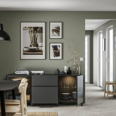 Moderní obývací prostor se šalvějově zelenými stěnami, tmavou dřevěnou skříňkou, stylizovanou s vázami, s minimalistickým, elegantním designem.