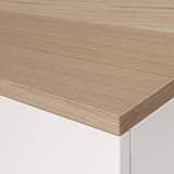 Detailní záběr hladké, světlé dřevěné desky stolu s bílou základnou, která předvádí přirozenou kresbu a čistý povrch.