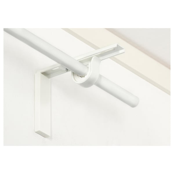 Bílý nastavitelný držák záclonové tyče namontovaný na bílé stěně. Umožňuje všestranné možnosti zavěšení záclon blízko nebo daleko od okna.