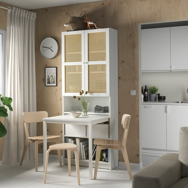 Moderní jídelní kout s bílou knihovnou BILLY s psacím stolem, židlemi ze světlého dřeva, šedou pohovkou a kuchyňskou linkou u dřevěné stěny.