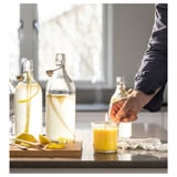 Muž zapaluje u okna žlutou svíčku BLODHÄGG. Na prkénku sedí dvě skleněné nádoby s plátky citronu. Světlá, prosluněná kuchyňská scéna.