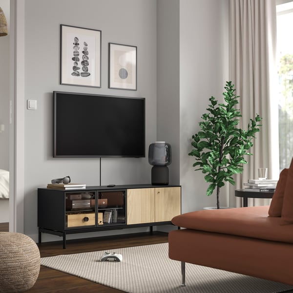 Moderní obývací pokoj s černým a dřevěným tv stolkem, skleněnými dveřmi, tv nahoře, oranžovou pohovkou, rostlinou.