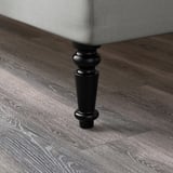 Detailní záběr na nohu nábytku vyrobenou z leštěného černého dřeva s hladkým, lesklým povrchem.