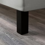 Detailní záběr na robustní nohu postele z tmavého dřeva, která předvádí její hladký povrch a pevnou konstrukci.