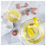 Napůl nakrájený citron v odšťavňovači vedle skleněné nádoby se žlutými citrusovými slupkami; dřevěné kusy v blízkosti.