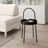 Moderní minimalistický černý kulatý odkládací stolek u bílé pohovky, drží podnos a misku, má praktickou rukojeť.