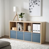 Minimalistický obytný prostor se světlým dřevem a modrým úložným dílem. Jsou v něm knihy, lampa a rostliny. Rámeček je úzký, vejde se pod kresbu.