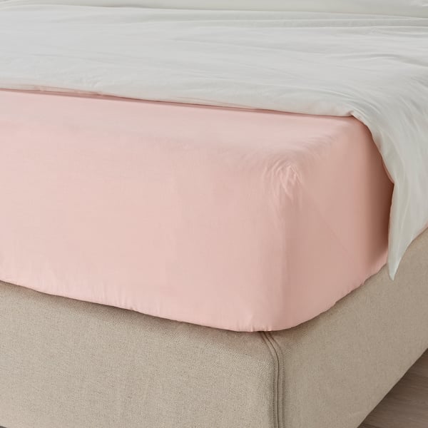 Postel se světle růžovým elastickým prostěradlem, vyrobené z bavlny pro prodyšnost, s elastickými okraji pro bezpečné uchycení.