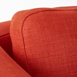 Detailní záběr na oranžovou židli z měkké látky, která předvádí její robustní prošívání a plyšovou texturu.