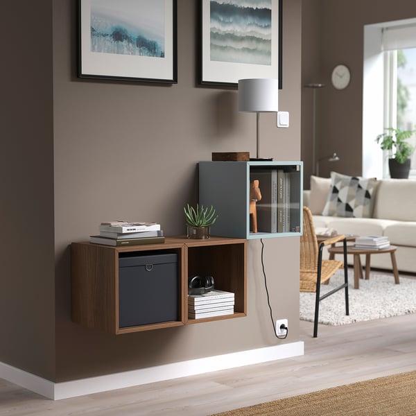 Úložný díl EKET se skleněnými dveřmi, modrý koš, knihy, sluchátka, rostlina. Moderní, minimalistický obytný prostor.