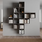 Moderní nástěnná šedá knihovna, naplněná knihami a dekorativními předměty. Asymetrický design s více přihrádkami.