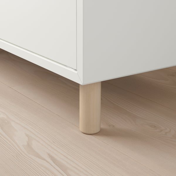 Moderní bílá skříň s dřevěnými nohami na světlé podlaze.