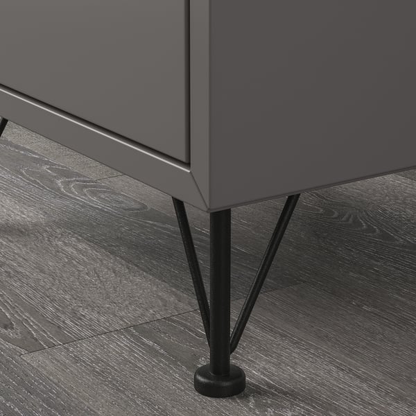 Tmavě šedý úložný díl na dřevěné podlaze s tenkými černými kovovými nohami pro stabilitu a elegantním designem.