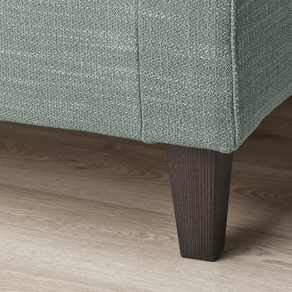 Detail stylového, čalouněného koutu pohovky s tmavou dřevěnou nohou na dřevěné podlaze.