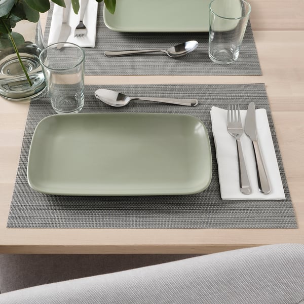 Zelený obdélníkový talíř se lžící, vidličkou, sklenicí a ubrouskem na prostírání.