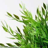 Jasně zelené, živé listy umělé rostliny, pečlivě propracované s kapičkami vody na každém z nich, uspořádané přirozeným, huňatým způsobem.