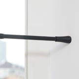 Černá nastavitelná tyč na závěsy namontovaná na bílé stěně, sahající od 70 do 120 cm, s gumovými krytkami na koncích, které zabraňují poškrábání.