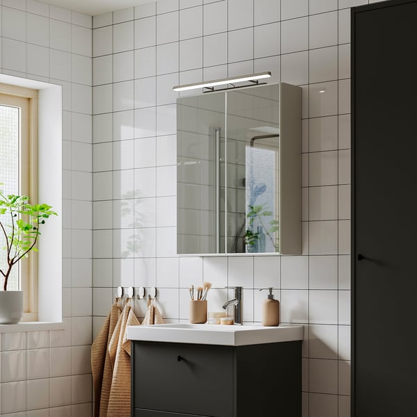 Moderní koupelna s chromovým LED světlem FLASKPOST nad zrcadlem, odrážející marnost s béžovými ručníky a dekorem.