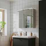 Moderní koupelna s osvětleným zrcadlem, chromem, tmavým umyvadlem, rostlinami odrážejícími přirozené světlo.