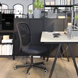 Moderní černé kancelářské uspořádání: ergonomická židle, stůl, knihovna s rostlinami a lampa.