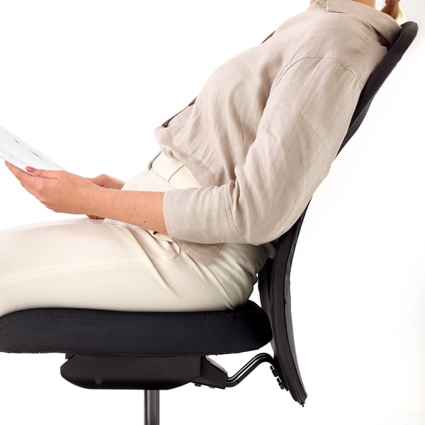Osoba sedící na ergonomické kancelářské židli, opřená o opěradlo s dobrou bederní opěrkou. Vidět je opěradlo ze síťoviny a nastavení židle.