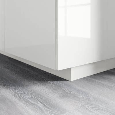 Bílý lesklý sokl kuchyňské linky na dřevěné podlaze.