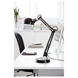 Černá nastavitelná stolní lampa na bílém stole vedle počítačového monitoru a skla.