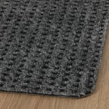 Šedá rohožka s texturovaným povrchem, umístěná na dřevěné podlaze, vynikající svým odolným a stylovým designem.