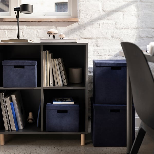 Minimalistická domácí kancelář s úložnými krabicemi GJÄTTA v modrém sametu, knihami a elegantním nábytkem.