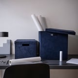 Moderní uspořádání psacího stolu s úložnými boxy GJÄTTA v modré barvě, rozměry vedle papíru A4 a poznámkové bloky pro měřítko. Dekorativní a funkční.