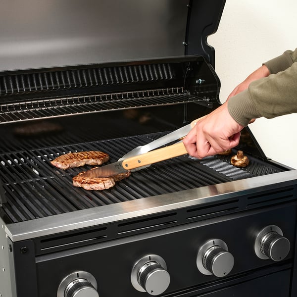 Osoba grilující steak pomocí kleští na plynovém grilu.