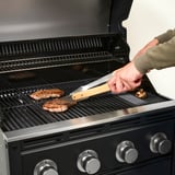 Osoba grilující steak pomocí kleští na plynovém grilu.